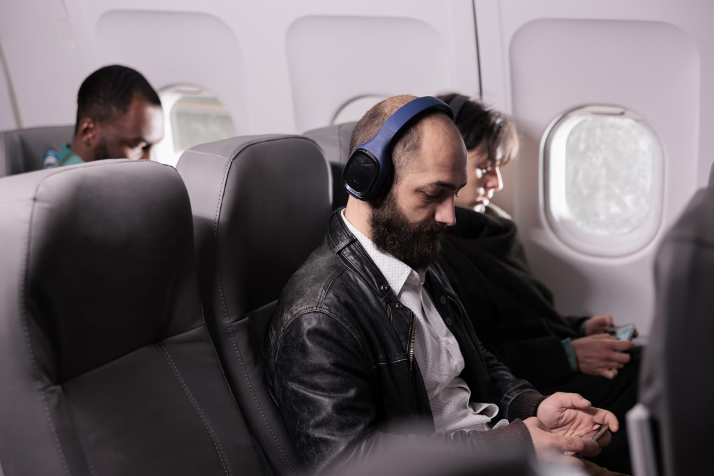 Passenger wearing Sony WH-1000XM5 headphones on a plane, enjoying a quiet and comfortable flight with noise cancellation.